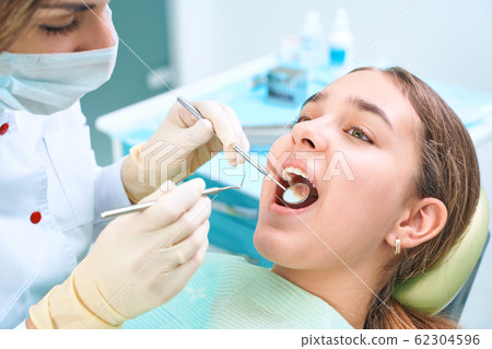Girl sitting at dental chair with open mouth during oral check up while doctor. Visiting dentist office. Dentistry concept. Girl sitting at dental chair with open mouth during oral check up while doctor. Visiting dentist office. Dentistry concept. 62304596