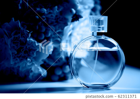 A round bottle of perfume on a dark background, near a bouquet with pink flowers.Aromatherapy and perfumes. Classic blue. The 2020 trend. 62311371