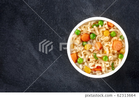 Ramen cup, instant soba noodles in a plastic cup, with green peas and carrot, overhead shot with a place for text on a black background 62313664
