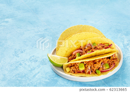 Cochinita pibil taco shells, a Mexican snack with pulled pork and avocado and marinated red onion, a close-up shot on a blue background with copy space 62313665