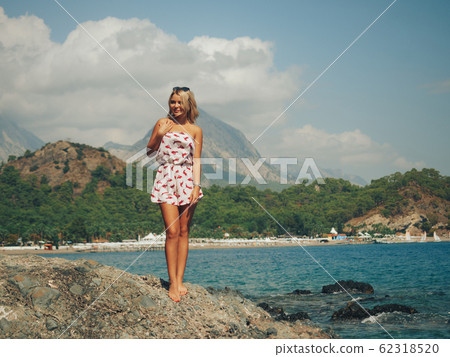 Young woman standing on the rocks by the sea Young woman standing on the rocks by the sea 62318520