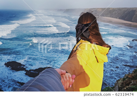 Young woman holding male hand on the hill with view to the ocean. Young woman holding male hand on the hill with view to the ocean. 62319474