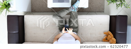 Man sit on sofa and hold modern smartphone in hand Man sit on sofa and hold modern smartphone in hand 62320477