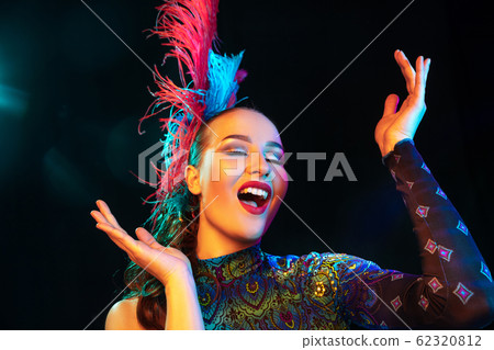 Beautiful young woman in carnival and masquerade costume in colorful neon lights on black background 62320812