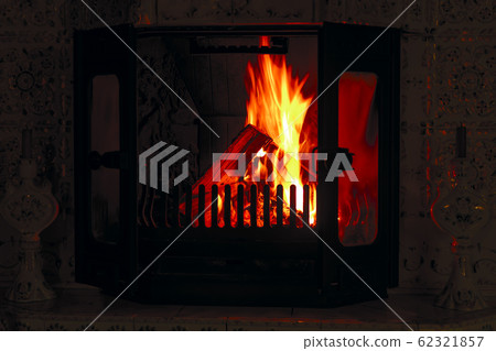 Burning logs in ancient fireplace with tiles.  62321857