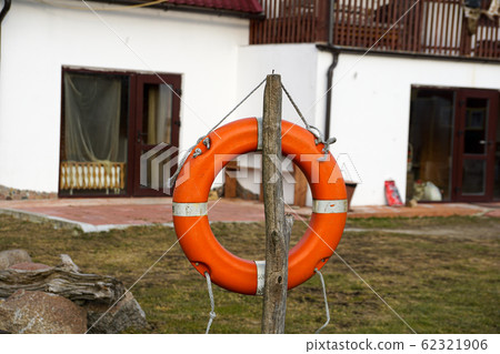An orange lifebuoy hangs on a log against the background of the house and lawn. 62321906