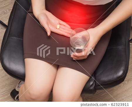 Girl holds a glass of water and a pill on a background of the abdomen. The concept of painkillers for menstruation and abdominal pain in women 62323911