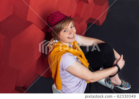 The girl in the red hat sits near the red wall The girl in the red hat sits near the red wall 62330349