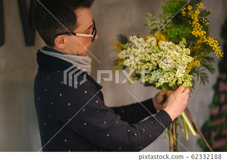 Flowers delivery shop. Florist creating order, making spring bouquet. Male make bouquet using yellow tulips and lilac Flowers delivery shop. Florist creating order, making spring bouquet. Male make bouquet using yellow tulips and lilac 62332188