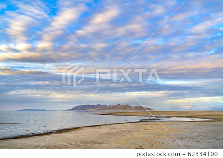 Gleaming lake with sandy shore and rugged mountain 62334100