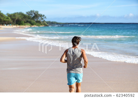 Man athlete running away from behind on beach at sunset. Male runner doing cardio exercise workout on sand with ocean background. Healthy active life on travel destination Man athlete running away from behind on beach at sunset. Male runner doing cardio exercise workout on sand with ocean background. Healthy active life on travel destination 62340592