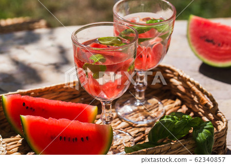 On a table in the garden in a basket are two glasses of lemonade and sliced of watermelon On a table in the garden in a basket are two glasses of lemonade and sliced of watermelon 62340857