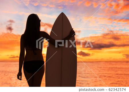 Beach sunset sexy surfer woman surfing lifestyle relaxing holding surfboard looking at ocean waves for surf. Active healthy living silhouette of sports athlete standing in colorful sky Beach sunset sexy surfer woman surfing lifestyle relaxing holding surfboard looking at ocean waves for surf. Active healthy living silhouette of sports athlete standing in colorful sky 62342574