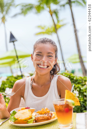 Happy woman at restaurant eating Hawaii burger with pineapple and karaage fried chicken. Hawaiian japanese fusion food. Asian girl at hotel restaurant table during summer travel vacation 62344438