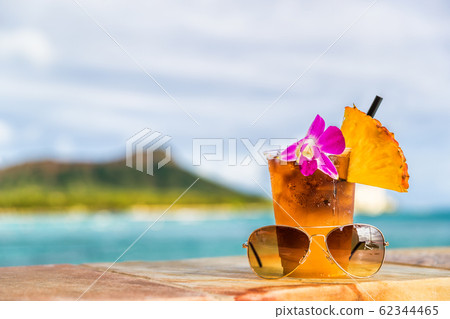 Hawaii mai tai cocktail drink on waikiki beach bar with flower, pineapple and sunglasses. View of the ocean and diamond head mountain in Honolulu, Hawaii. Summer vacation 62344465