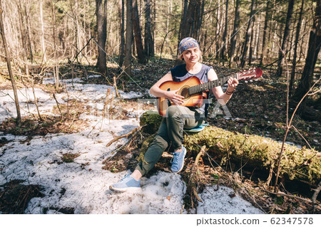 Young woman playing guitar sitting on old tree covered with moss at sunny spring forest Young woman playing guitar sitting on old tree covered with moss at sunny spring forest 62347578