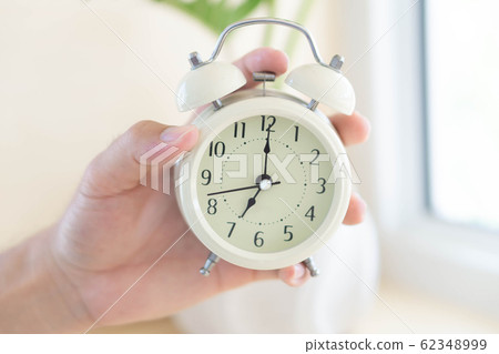 Closeup hand holding alarm clock on table Closeup hand holding alarm clock on table 62348999