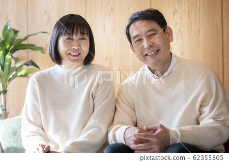 一對夫婦在他們50多歲的時候並排坐在沙發上。 一對夫婦在他們50多歲的時候並排坐在沙發上。 62355805
