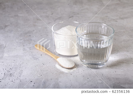 Collagen protein powder - Hydrolyzed. Spoon and glass of water. Collagen protein powder - Hydrolyzed. Spoon and glass of water. 62356136