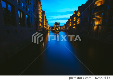 Wide perspective of Warehouse District - Speicherstadt in twilight. Blue hour. Tourism landmark of Hamburg. View of Wandrahmsfleet in light of lantern lamp in HafenCity 62359113