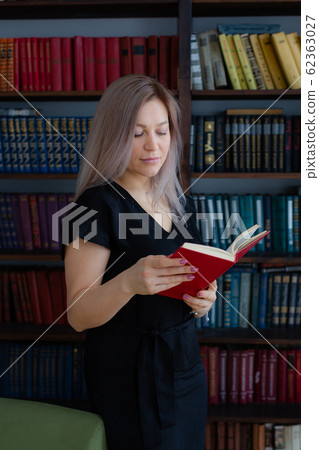 Blonde woman in a black dress in a library or in a cabinet. Blonde woman in a black dress in a library or in a cabinet. 62363027