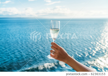 Champagne glass woman's hand toasting on ocean background at luxury cruise ship during sunset. Travel vacation for honeymoon, lady holding flute wearing wedding ring. Champagne glass woman's hand toasting on ocean background at luxury cruise ship during sunset. Travel vacation for honeymoon, lady holding flute wearing wedding ring. 62363153