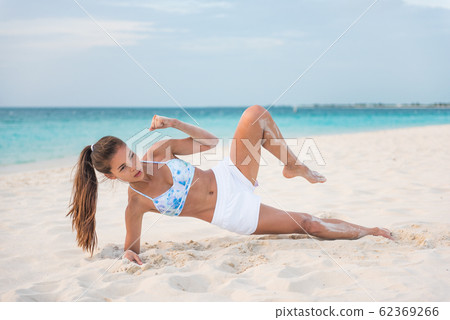 How to do a Side Plank Crunch fitness instruction demonstration physical trainer on beach training obliques stomach muscles doing core body training. Fit girl exercising doing abs exercise 62369266