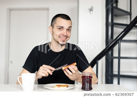 The guy has breakfast with toast with jam. The guy has breakfast with toast with jam. 62369307