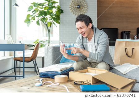 年輕人看著計算器試圖把不需要Mercari的衣服 62370741