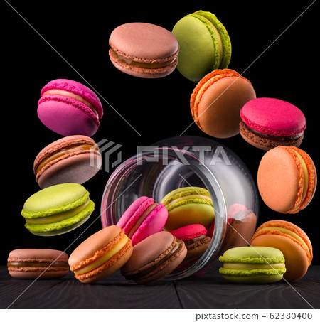 Flying french colorful macaroons and jar on wooden table isolated on black Flying french colorful macaroons and jar on wooden table isolated on black 62380400
