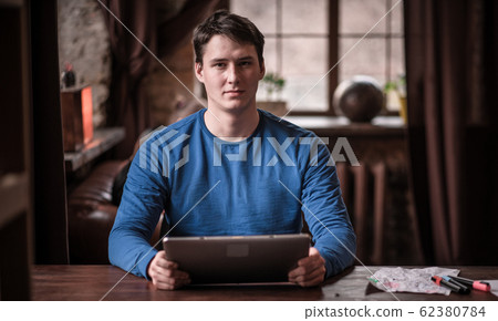 Serious Young Man Uses His Tablet While Working In Cozy Coworking Space. Serious Young Man Uses His Tablet While Working In Cozy Coworking Space. 62380784