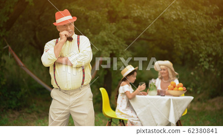 Oldman in park posing for camera across his family. 62380841