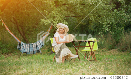 Old Lady sits in garden across hamack. Old Lady sits in garden across hamack. 62380842