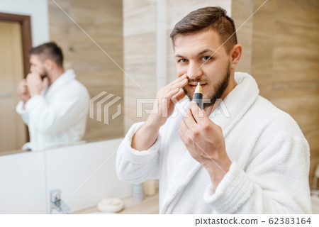 Man removes nose hair in bathroom, morning hygiene Man removes nose hair in bathroom, morning hygiene 62383164