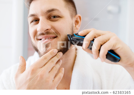 Man shaves his beard with an electric razor Man shaves his beard with an electric razor 62383165