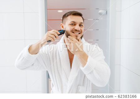 Man shaves his beard with an electric razor Man shaves his beard with an electric razor 62383166