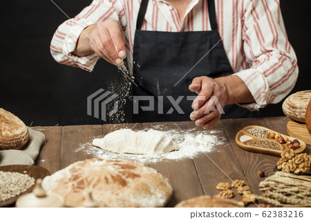 Man sprinkling some flour on dough. Hands kneading dough, cropped view 62383216