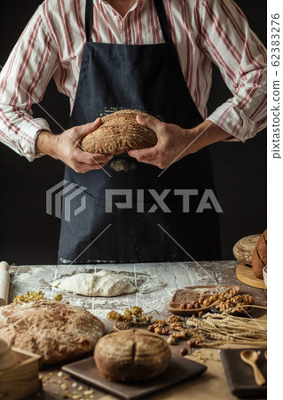 Unrecognizable baker holds freshly baked rustic organic loaf of bread in hand 62383276