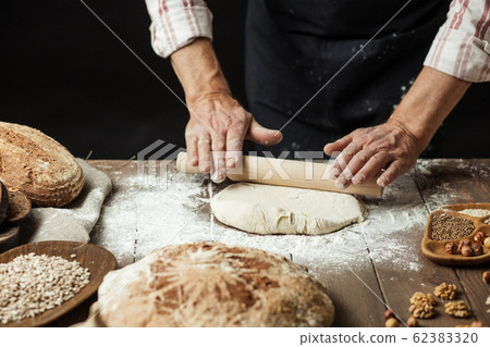 Close up of baker hands kneading dough and making bread with a rolling pin. Close up of baker hands kneading dough and making bread with a rolling pin. 62383320