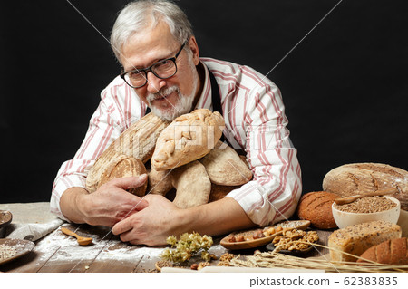 Happy old baker looking at camera and smiling while hugging loaves of bread Happy old baker looking at camera and smiling while hugging loaves of bread 62383835