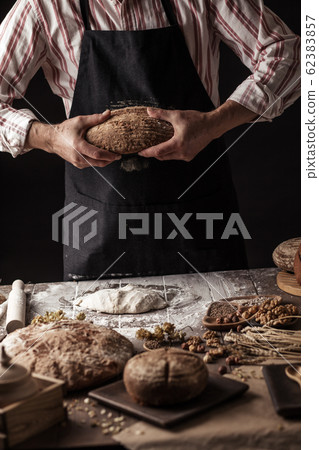 Unrecognizable baker holds freshly baked rustic organic loaf of bread in hand 62383857