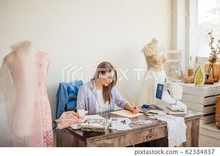 Fashion designer at work. Talanted dressmaker drawing sketch at her workspace Fashion designer at work. Talanted dressmaker drawing sketch at her workspace 62384837