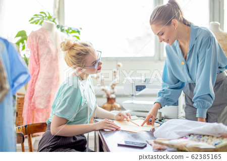 Female seamstress discussing features of the order with client in cozy studio Female seamstress discussing features of the order with client in cozy studio 62385165