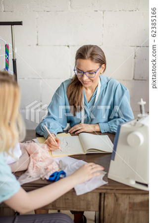 Female seamstress discussing features of the order with client in cozy studio Female seamstress discussing features of the order with client in cozy studio 62385166