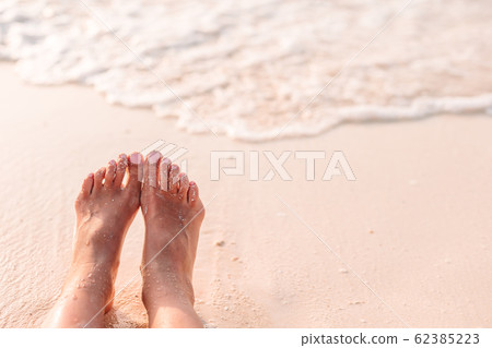 Woman's feet on the white sand beach in shallow water Woman's feet on the white sand beach in shallow water 62385223