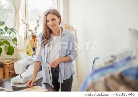 Beautiful seamstress is working with a wedding dress model in her studio 62385446
