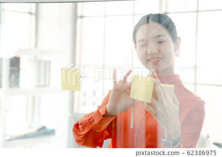 Woman using sticky notes on glass wall Woman using sticky notes on glass wall 62386975