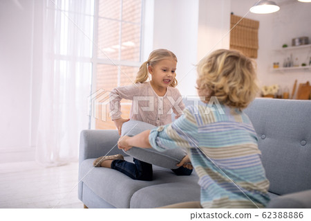 Two blond kids playing with grey sofa pillows 62388886