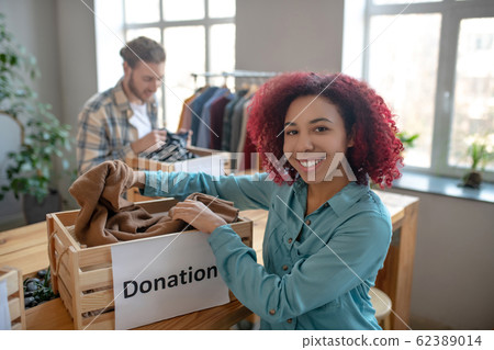 Young girl with curly burgundy hair folding clothes in drawer. Young girl with curly burgundy hair folding clothes in drawer. 62389014
