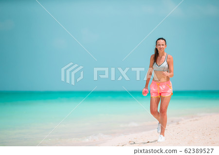 Fit young woman doing exercises on tropical white beach in her sportswear Fit young woman doing exercises on tropical white beach in her sportswear 62389527